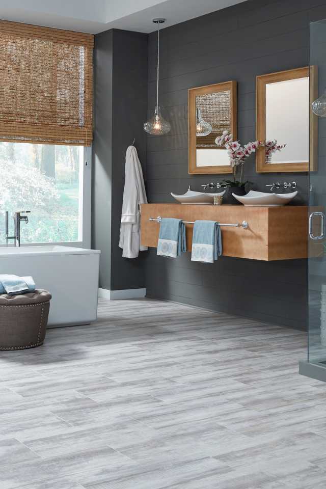 grey stone look luxury vinyl in modern bathroom with deep soak tub, grey walls and roman shades
